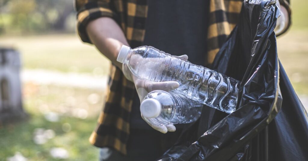 person putting water bottles into trash bag